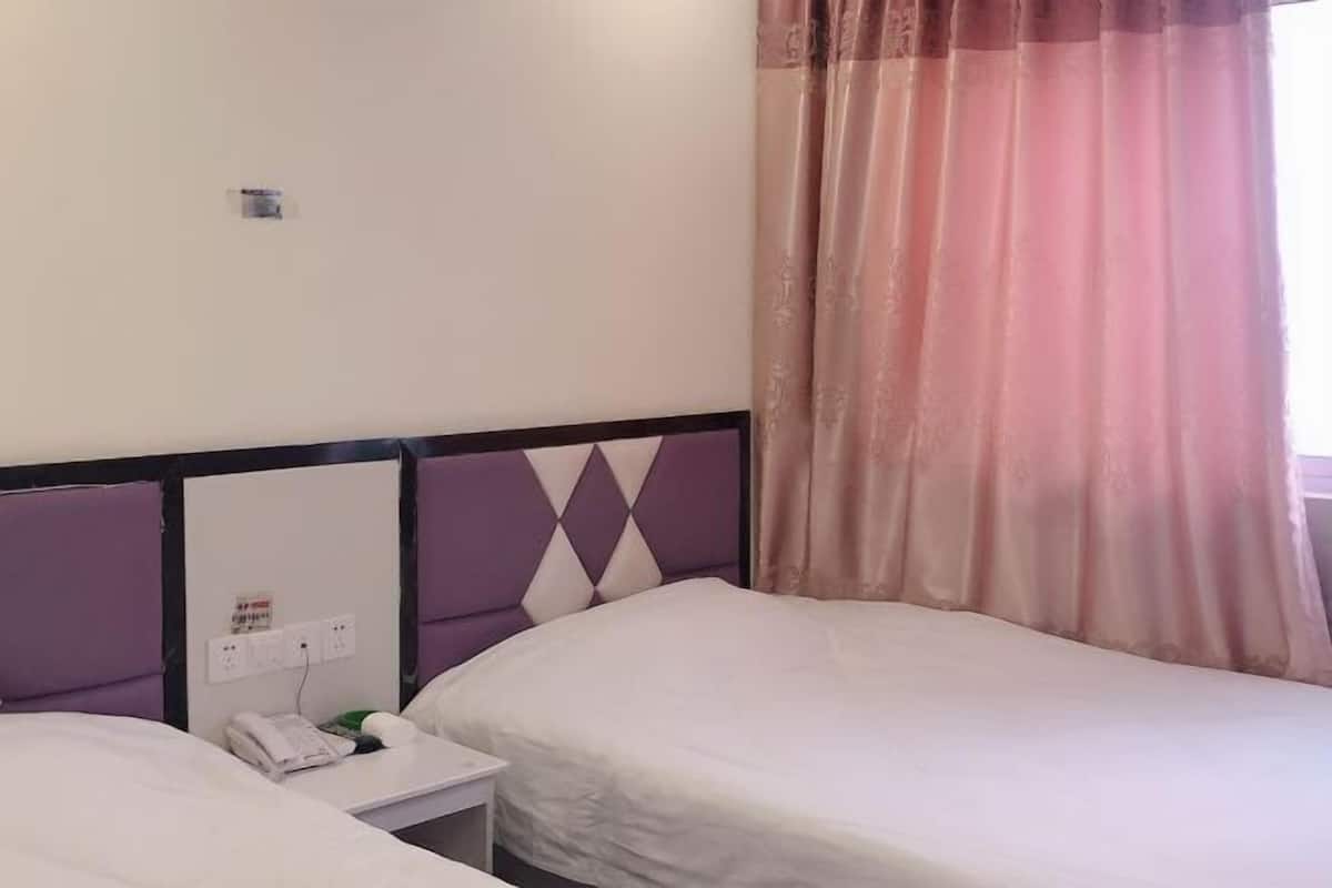 A hotel room with two beds, a nightstand, a power outlet, and a window with a curtain.