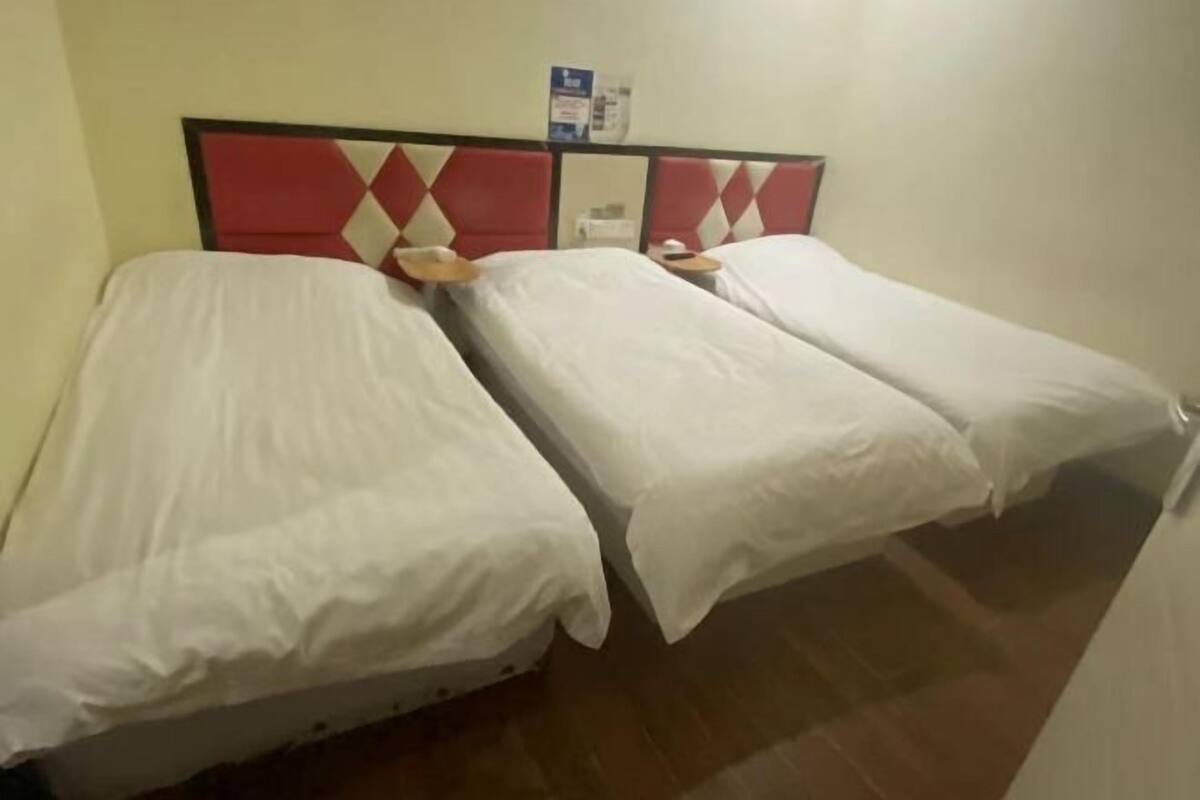 A hotel room with three single beds, a red and white headboard, and a small table between the beds.