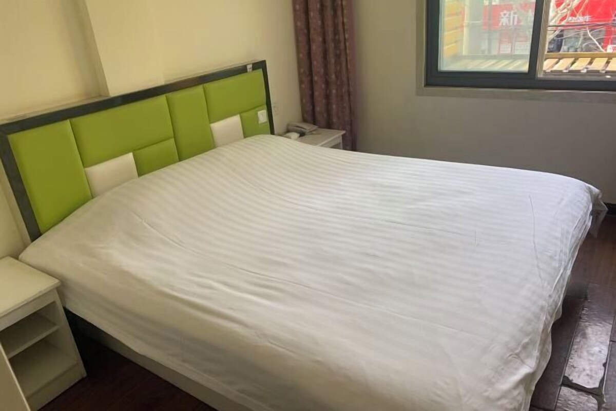 A bed with a green headboard and white bedding, a bedside table, and a window with curtains.
