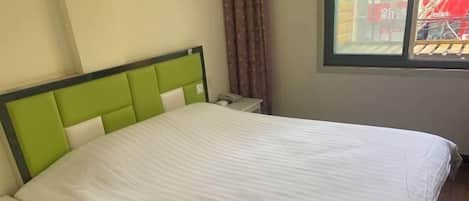 A bed with a green headboard and white bedding, a bedside table, and a window with curtains.