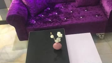 Um sofá roxo com uma almofada decorativa e um vaso de flores brancas sobre uma mesa preta.