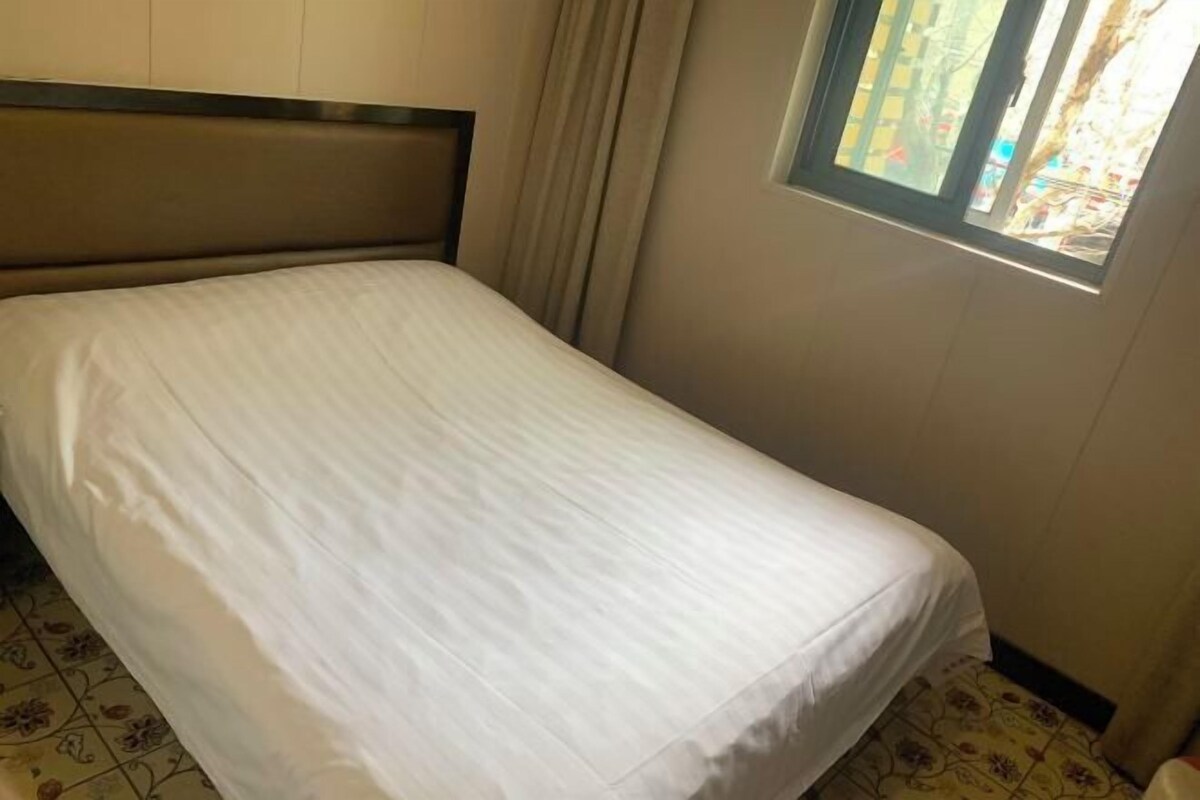A single bed with a headboard, a window with curtains, and patterned flooring.