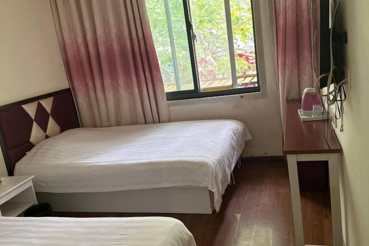 A room with two beds, a desk, and a window with curtains.