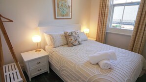 A neatly made bed with a patterned bedspread, two bedside lamps, a small bedside table with drawers, a framed picture on the wall, and a window with curtains. - Post Office Cottage Oakbank, Adelaide Hills Wine Region, Pikes Historic Brewery (Oakbank)