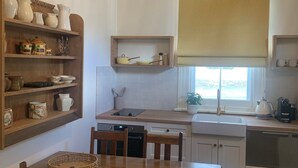 A kitchen with wooden cabinets, a dining table with chairs, a hanging light fixture, and a window with a blind. - Post Office Cottage Oakbank, Adelaide Hills Wine Region, Pikes Historic Brewery (Oakbank)