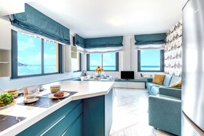 Eine moderne Küche mit einer zentralen Kochinsel, großen Fenstern mit Meerblick und einer Sitzecke mit Sofa und Fernseher.