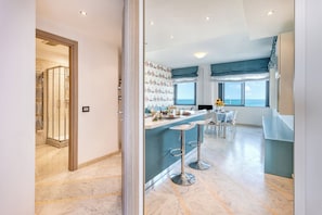 A modern kitchen with a bar area, a dining space, and a view of the sea.