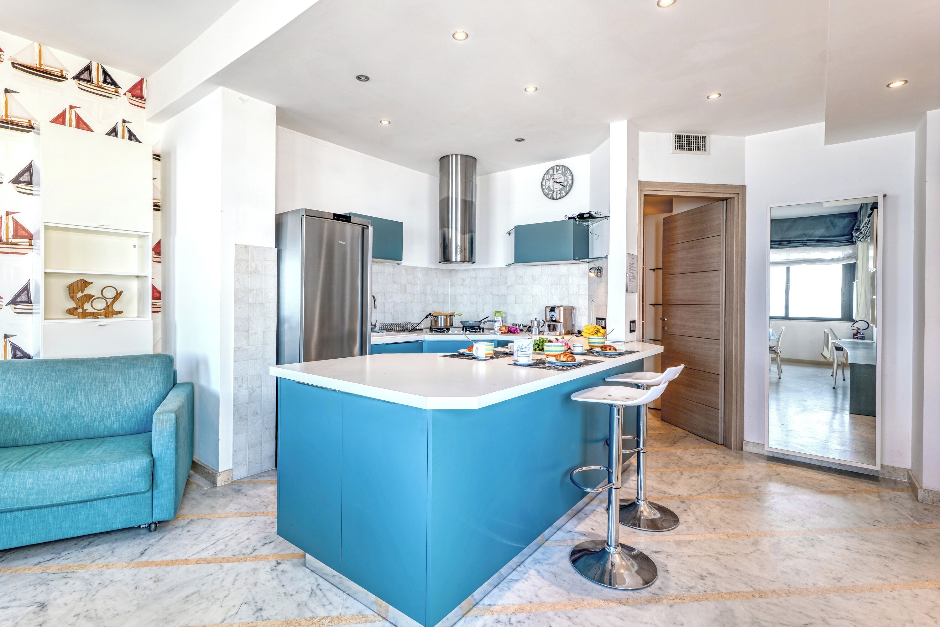 Eine moderne Küche mit einer blauen Kochinsel, Edelstahlgeräten und einem blaugrünen Sofa.