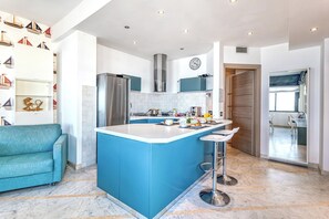 Una cocina moderna con una isla azul, electrodomésticos de acero inoxidable y un sofá verde azulado.