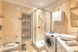 Ein Badezimmer mit Duschkabine, Waschmaschine, Waschbecken und Toilette.