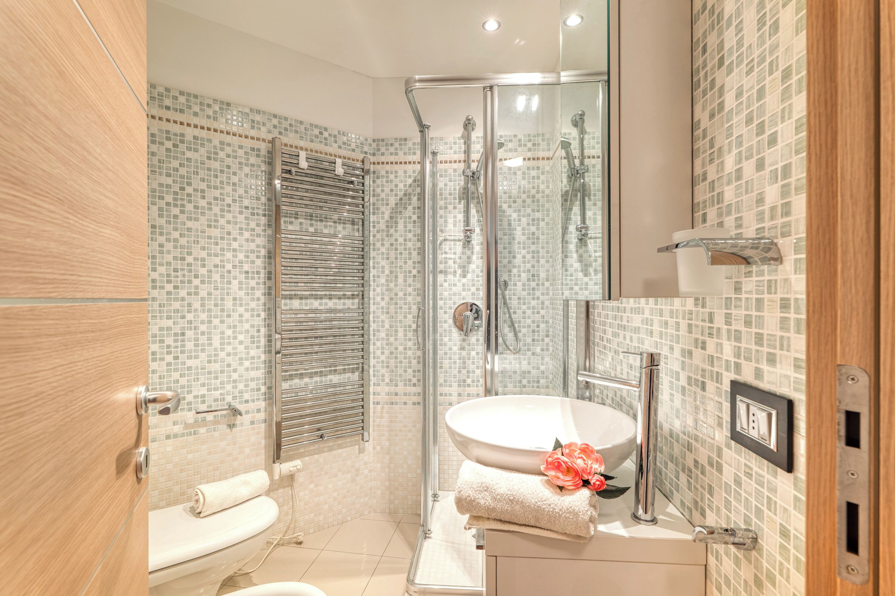 A bathroom with a glass shower enclosure, a sink with a rose decoration, and a toilet.