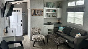 A compact living space with a kitchenette, a sofa, a coffee table, and a TV mounted on the wall.