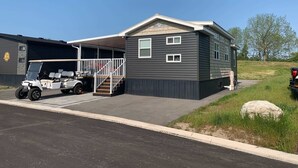 A mobile home with a covered garage, a golf cart, and a large rock in the foreground.