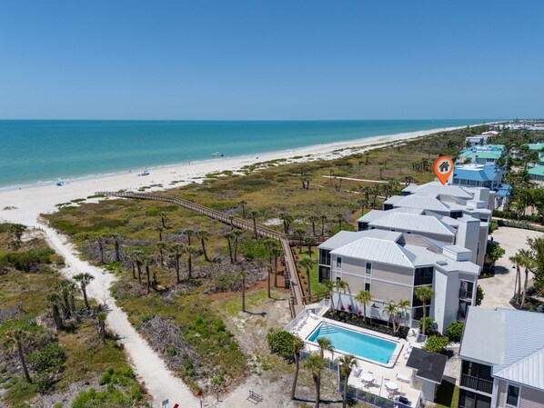 A coastal hotel with a beach view, a swimming pool, and a boardwalk leading to the beach.