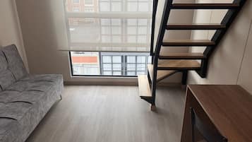 A room with a grey sofa, a wooden desk, and a black staircase.