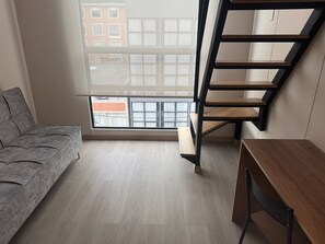 A room with a grey sofa, a wooden desk, and a black staircase. - Vivo52 (Bogotá)
