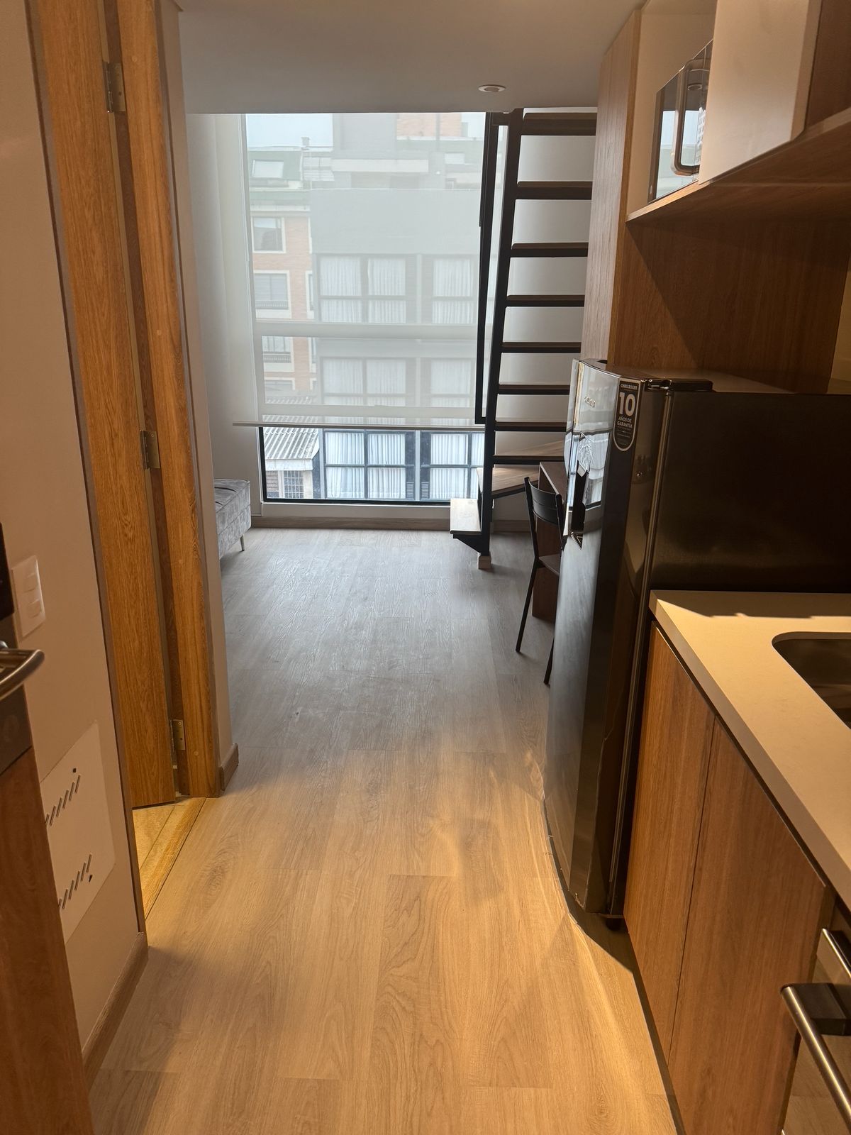A kitchen with a refrigerator, a wooden cabinet, and a window with a view of buildings.