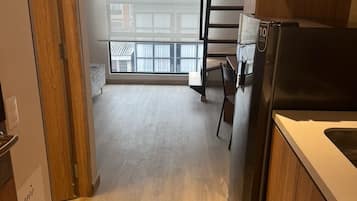 A kitchen with a refrigerator, a wooden cabinet, and a window with a view of buildings.