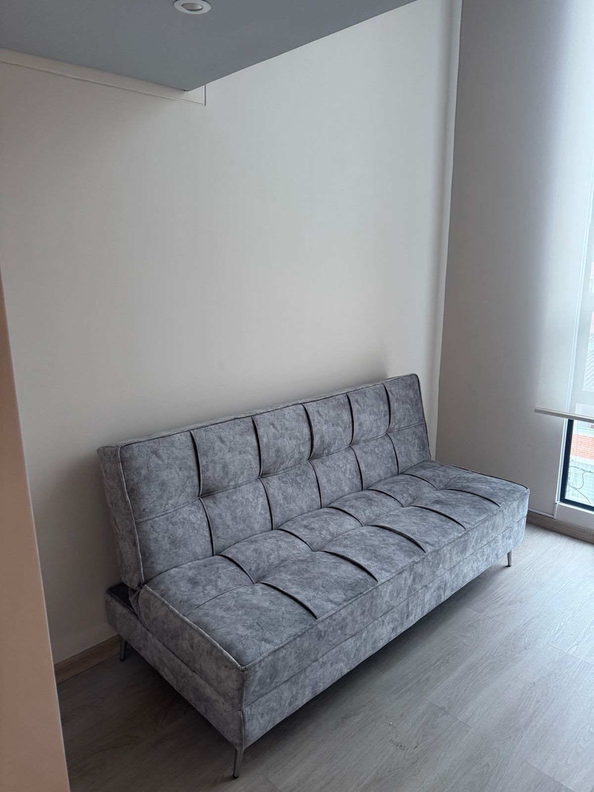 A grey sofa in a room with a plain white wall and a window.