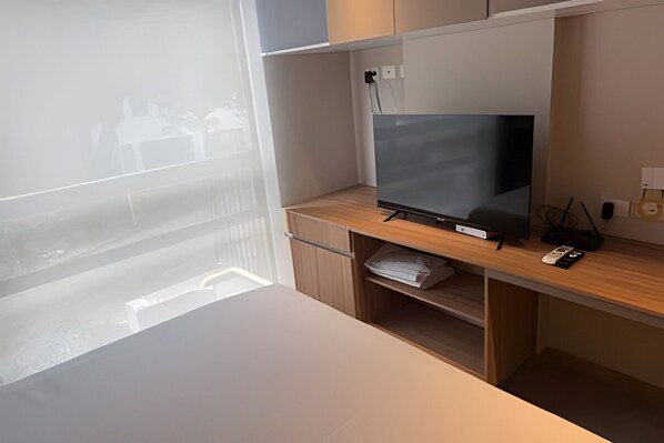 Una camera moderna con una grande finestra, una scrivania in legno, una TV a schermo piatto e uno scaffale con un telecomando.