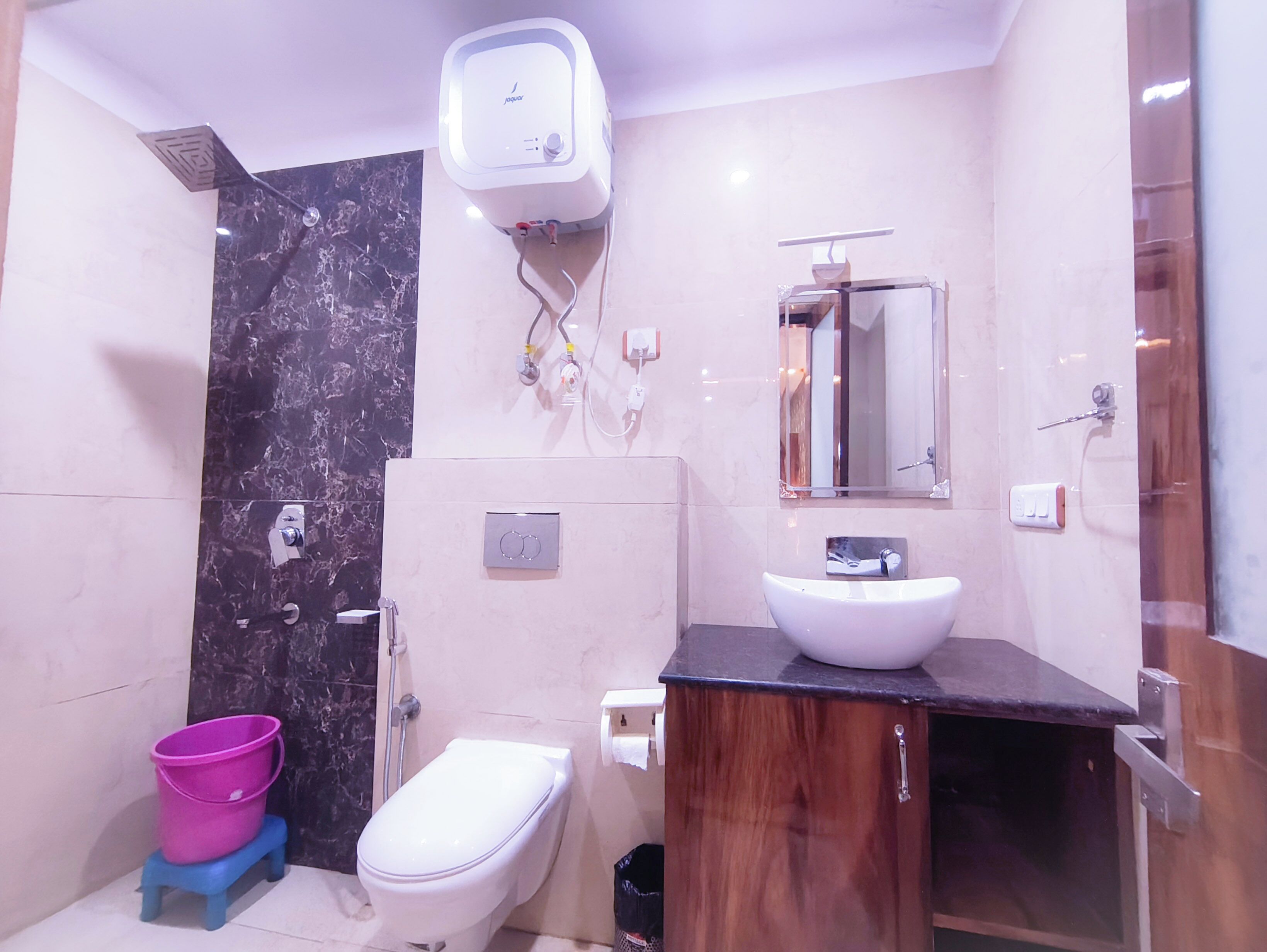 Un baño moderno con pared de mármol, inodoro blanco, tocador de madera y zona de ducha.