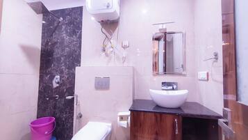 Un baño moderno con pared de mármol, inodoro blanco, tocador de madera y zona de ducha.