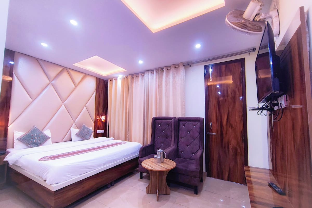 A hotel room with a large bed, a small round table, two armchairs, a TV, and a ceiling fan.