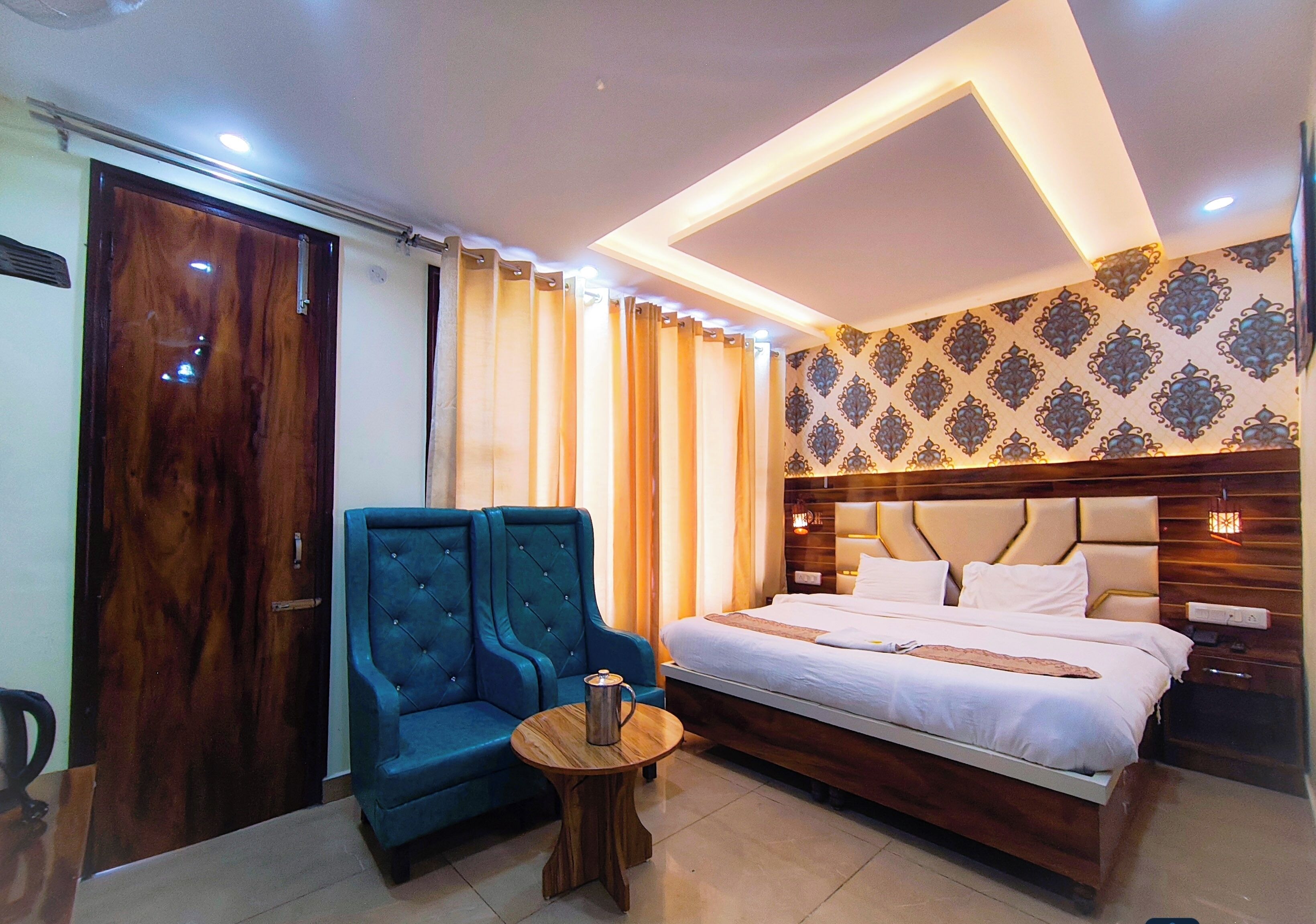 A hotel room with a large bed, a blue armchair, a small round table, and a wooden door.