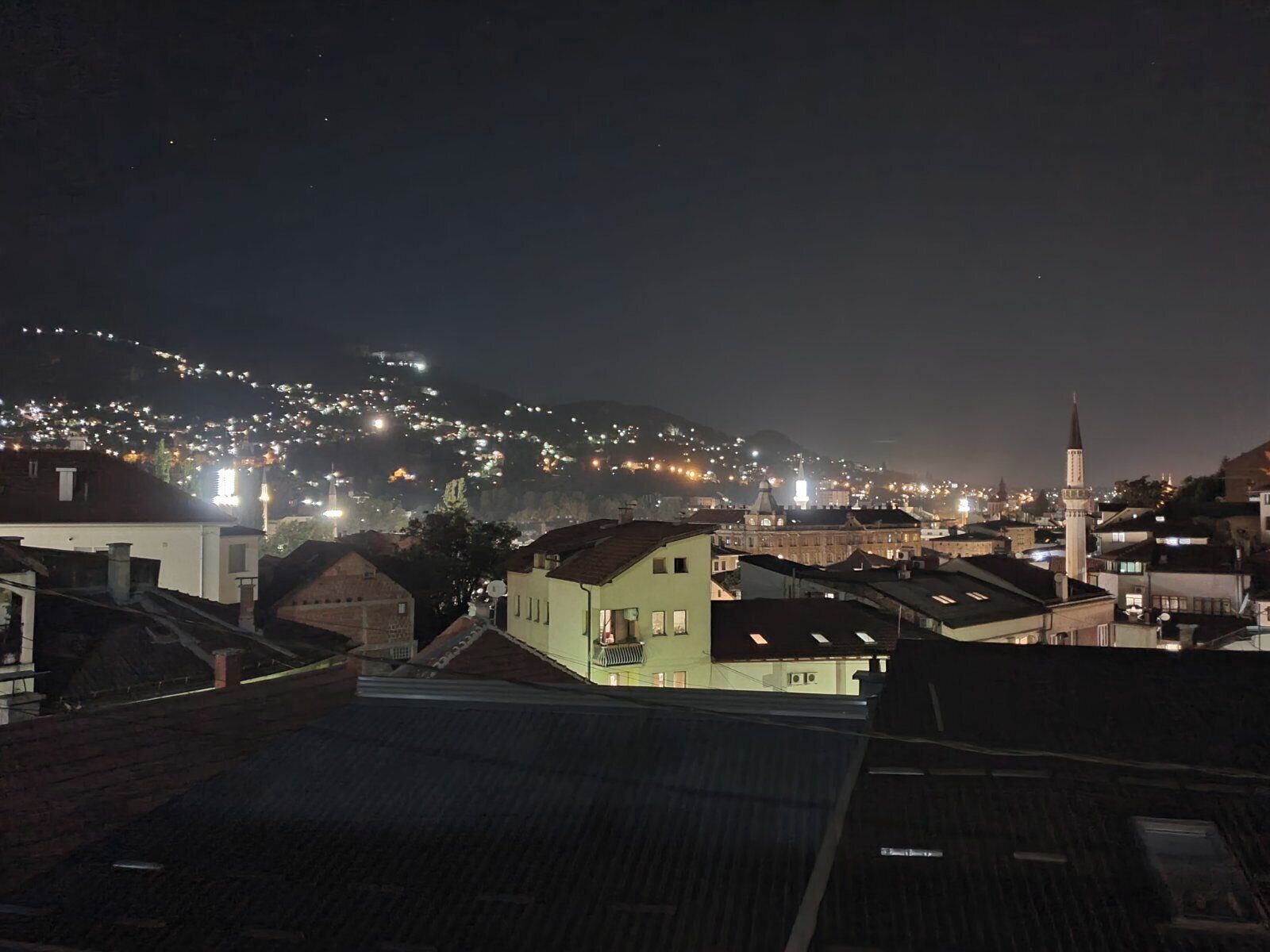 Vista nocturna de una ciudad con edificios iluminados y una mezquita destacada con un minarete.