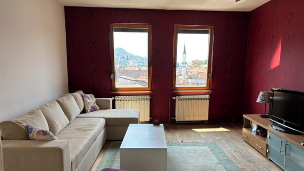 Un soggiorno con un divano, un tavolino, una TV e due finestre con vista sulla città.