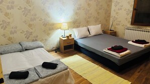 Camera da letto con due letti, un comodino con una lampada, un termosifone e carta da parati decorata.