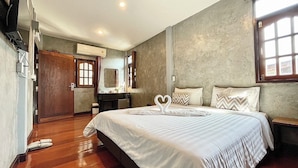 A bedroom with a large bed, wooden flooring, a wooden wardrobe, a mirror, and a window with curtains. - Momento House (Ayutthaya)