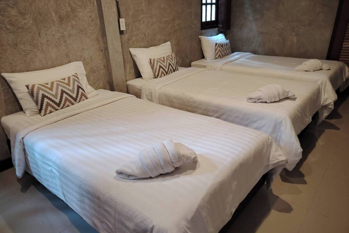 A hotel room with three single beds, each with a pillow and a blanket.