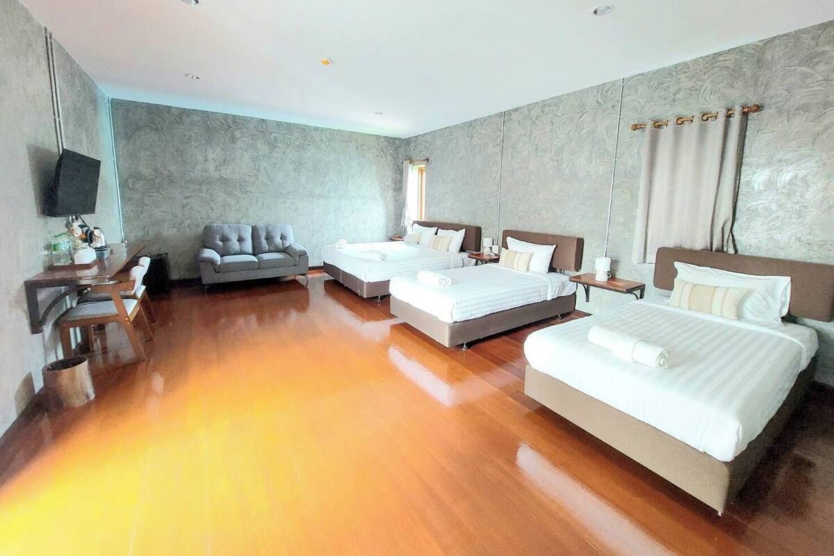 A hotel room with two beds, a sofa, a TV, and a wooden floor.