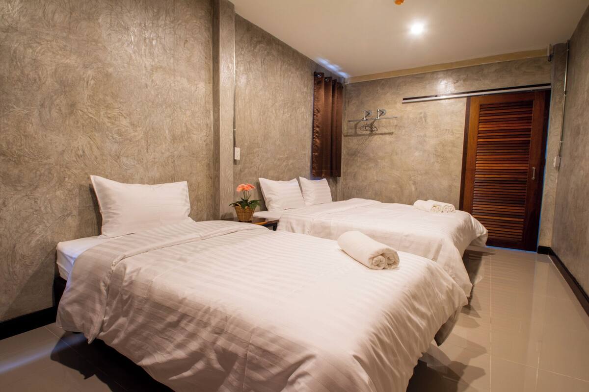 A hotel room with two beds, a wooden door, and a small table with a plant.