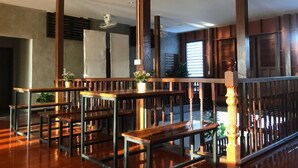 A spacious room with wooden furniture, including benches and a table, and a staircase with a wooden railing. - Momento House (Ayutthaya)