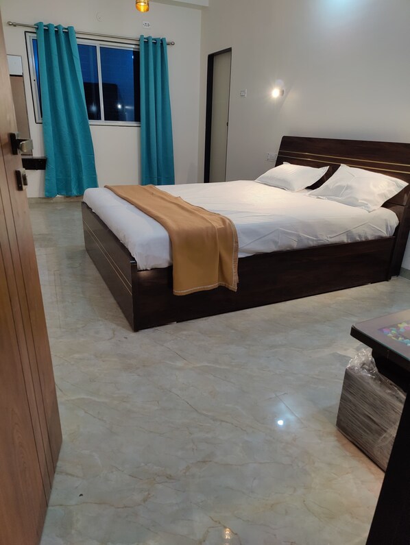 A bedroom with a bed, a wooden wardrobe, a window with curtains, and a nightstand. - Hotel Pearl (Akalkot)