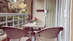 Een balkon met rieten meubilair, een tafel met een bloevas en een airconditioner.