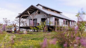 A rustic barn-style building with a sloped roof, large windows, and a wooden deck. - Stunningly built open-plan Studio in natural pastureland setting (Hay Valley)