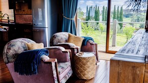 Un salon chaleureux avec un canapé et un fauteuil, une petite table d’appoint ronde et une vue sur l’extérieur.