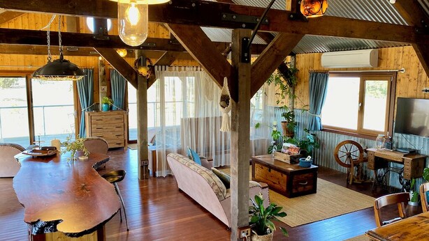 A rustic cabin interior with a wooden dining table, a sofa, a sewing machine, and a large window. - Stunningly built open-plan Studio in natural pastureland setting (Hay Valley)