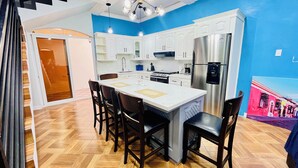 A modern kitchen with a central island, white cabinetry, stainless steel appliances, and a blue accent wall. - Lodging Vista hermosa (Esquipulas)