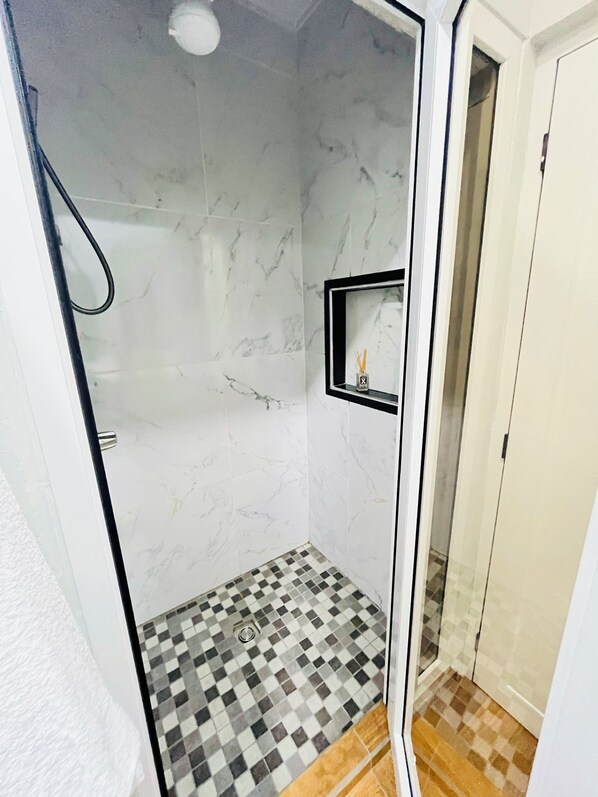 A walk-in shower with a checkered floor, a glass door, and a small shelf with a bottle.