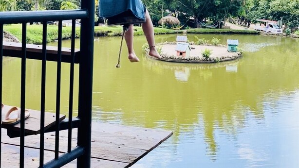 A person on a swing over a body of water with a forested hill in the background. - Lodging Vista hermosa (Esquipulas)