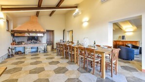 Un comedor amplio con una larga mesa de madera y sillas, piso de baldosas de piedra y una gran chimenea.