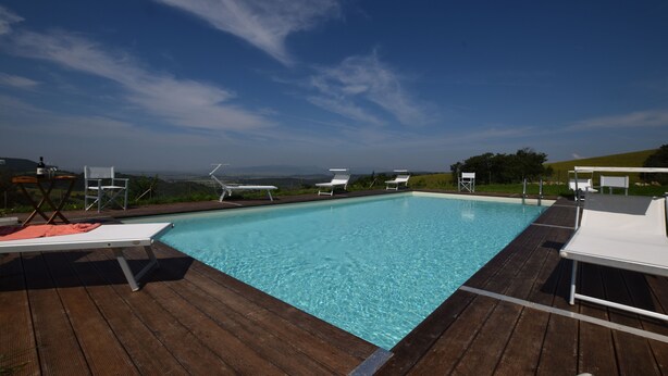 Una terraza de madera con piscina, sillones de descanso y vistas del paisaje.