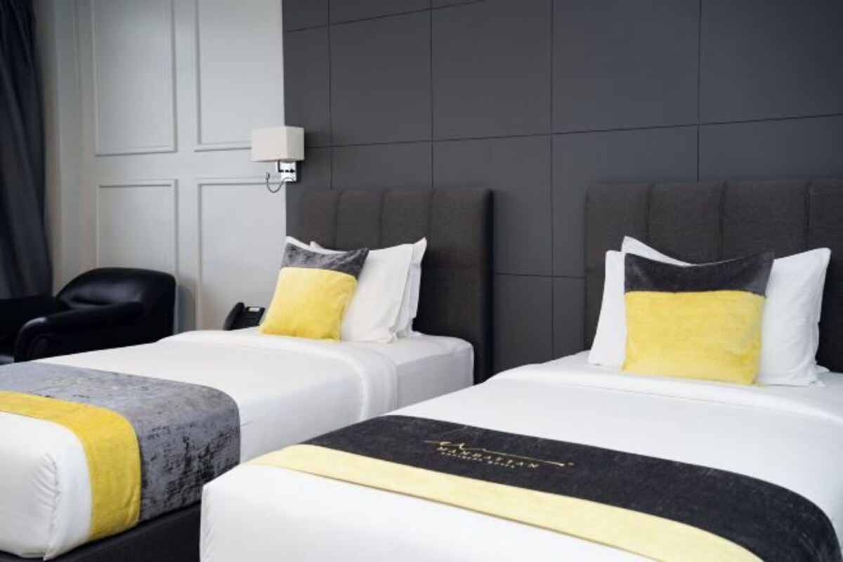 A hotel room with two beds, each with a white and gray headboard, and a black and yellow accent pillow.
