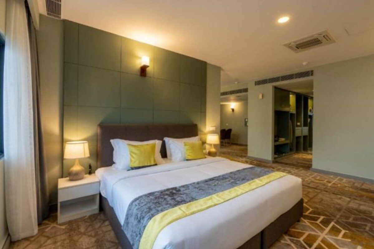 A hotel room with a large bed, nightstands with lamps, a headboard, and a patterned carpet.