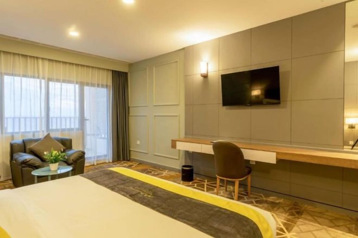 A hotel room with a bed, a desk, a chair, a TV, and a sofa.