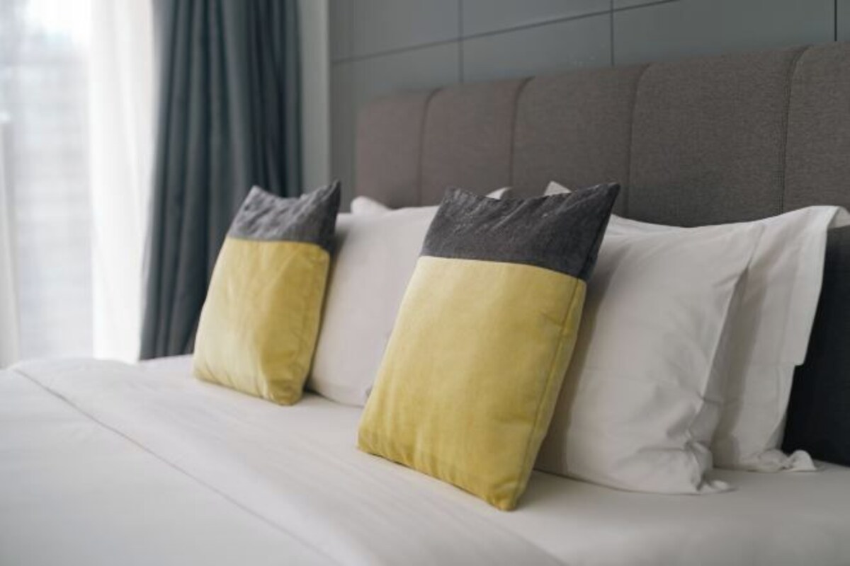 A bed with white bedding and two pillows, one with a yellow and gray design and the other plain white.